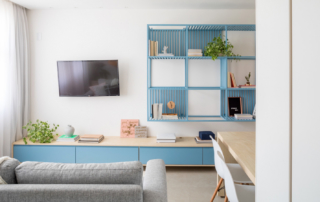 Sala de Estar da Residência, detalhes em branco, madeira e azul, poltrona, aparador e estante, com televisão na parede ao fundo